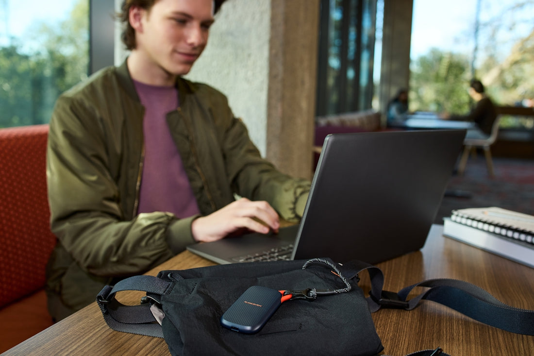 Young man uses laptop, portable storage device on table.