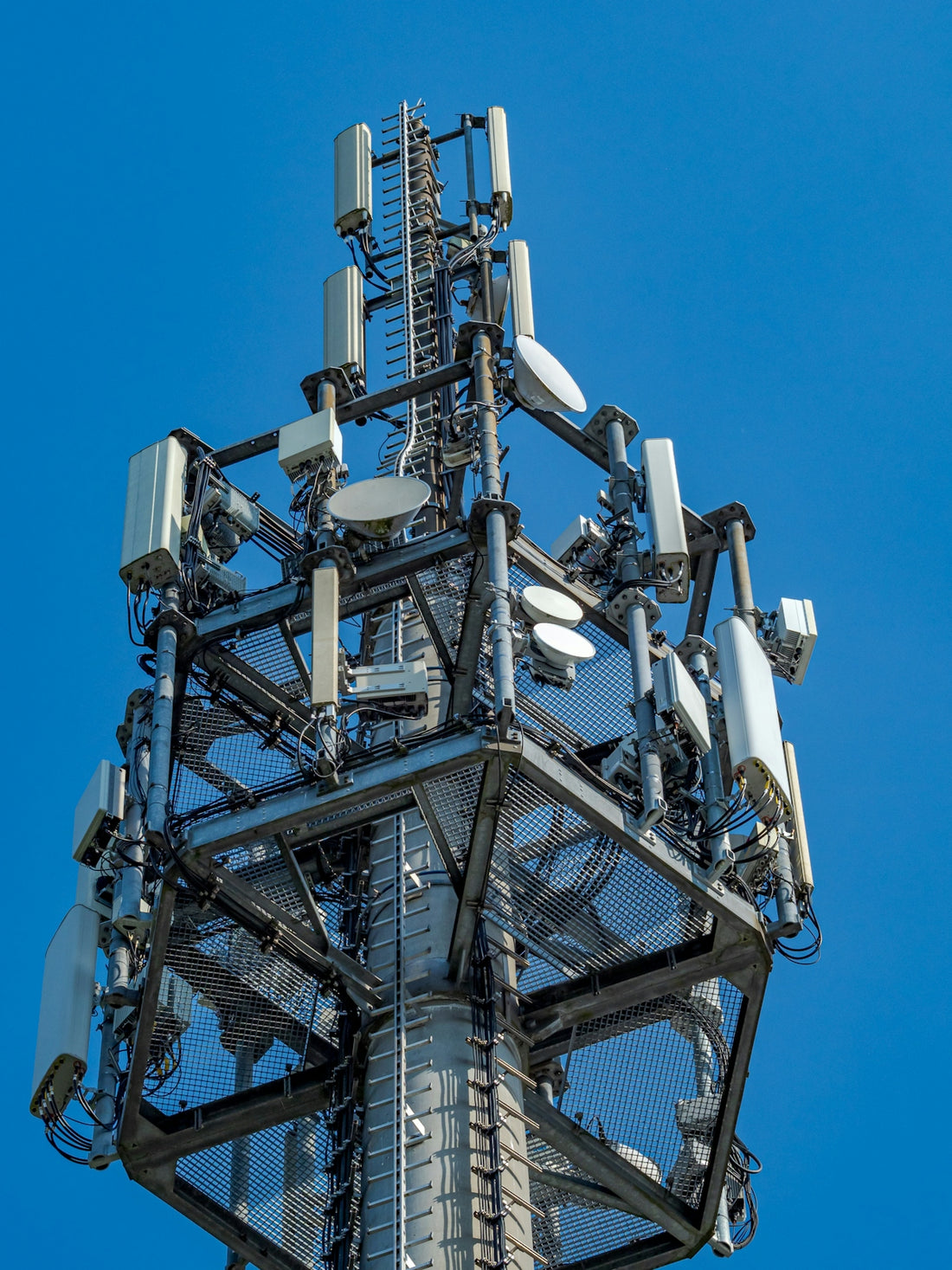 A tall telecommunications tower with many antennas against blue sky.